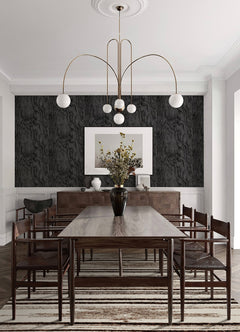 A modern bedroom features a dark, textured accent wall created with Ashley Stark Home Sloane Wood Peel and Stick Wallpaper by WallPops. A black upholstered bed with white bedding and a patterned pillow is complemented by a black nightstand that holds books, a towel, and a vase of pink flowers, all situated beneath a sleek wall-mounted lamp.
