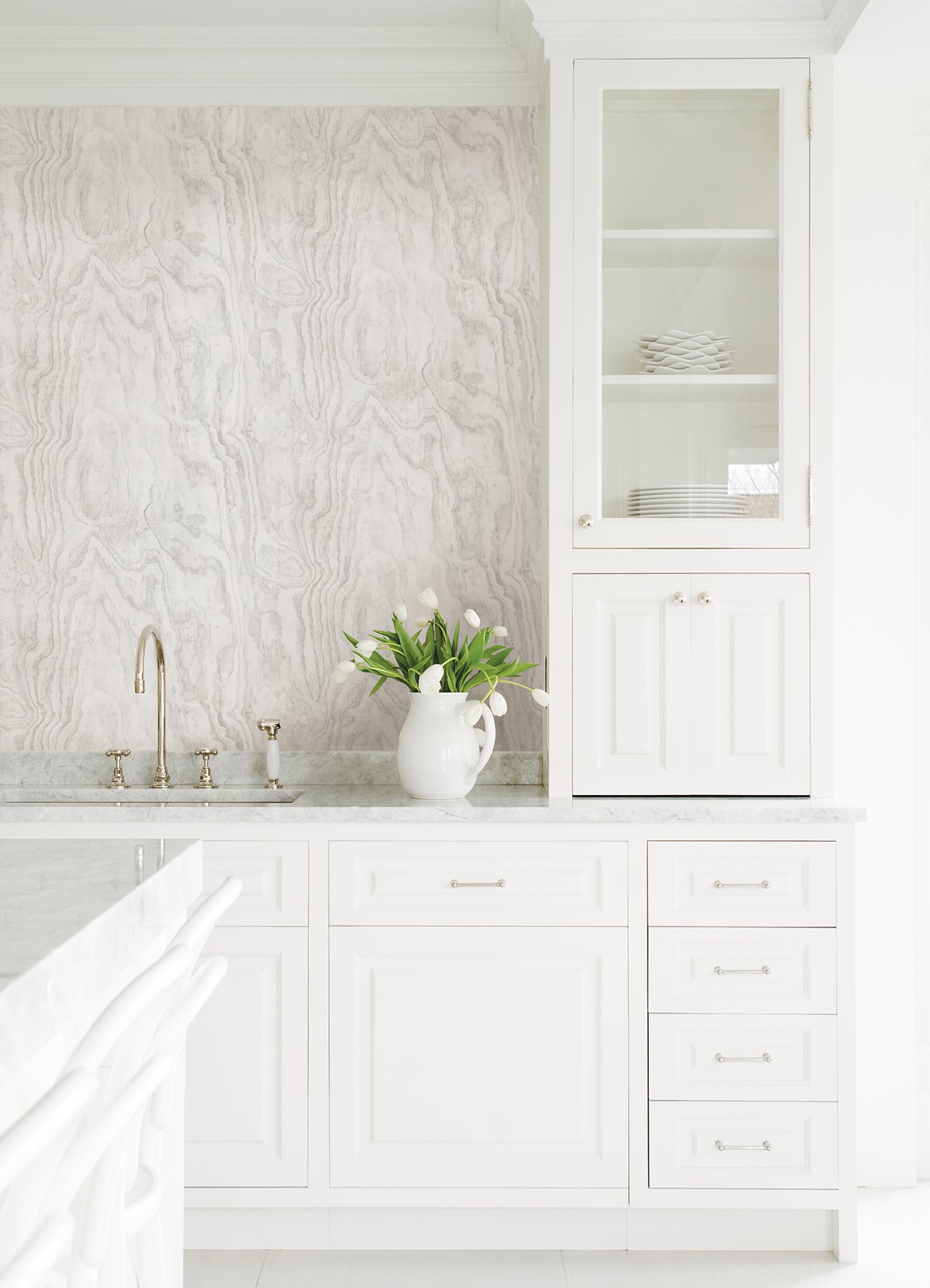 A modern bedroom features a dark, textured accent wall created with Ashley Stark Home Sloane Wood Peel and Stick Wallpaper by WallPops. A black upholstered bed with white bedding and a patterned pillow is complemented by a black nightstand that holds books, a towel, and a vase of pink flowers, all situated beneath a sleek wall-mounted lamp.