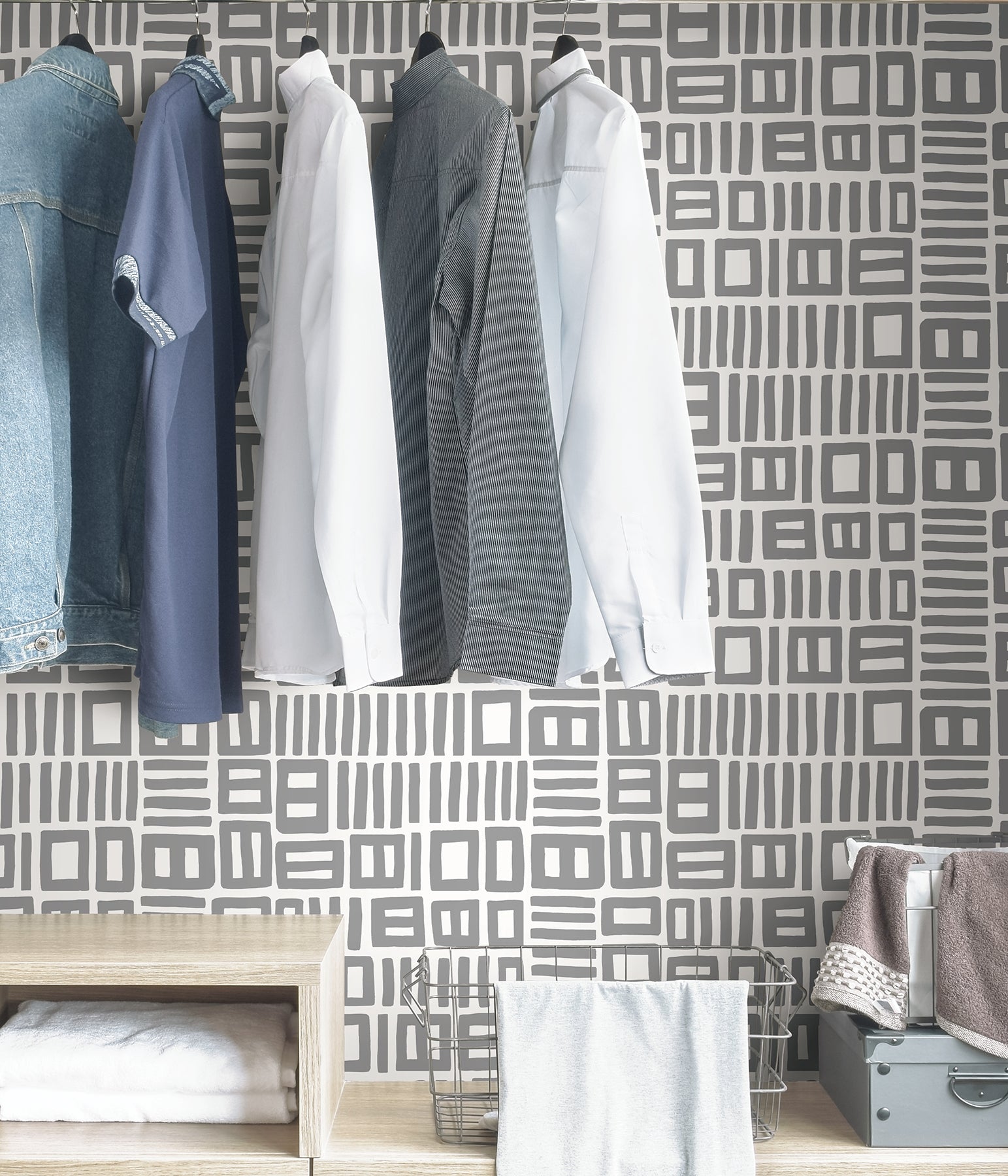 Beneath dark gray cabinets, a backsplash is enhanced with WallPops Black Pepper Paperie Traverse Peel and Stick Wallpaper, showcasing a bold geometric gray and white square pattern reminiscent of striking wallpaper. On the white countertop sit three white canisters with wooden lids alongside a large white bowl filled with green apples.