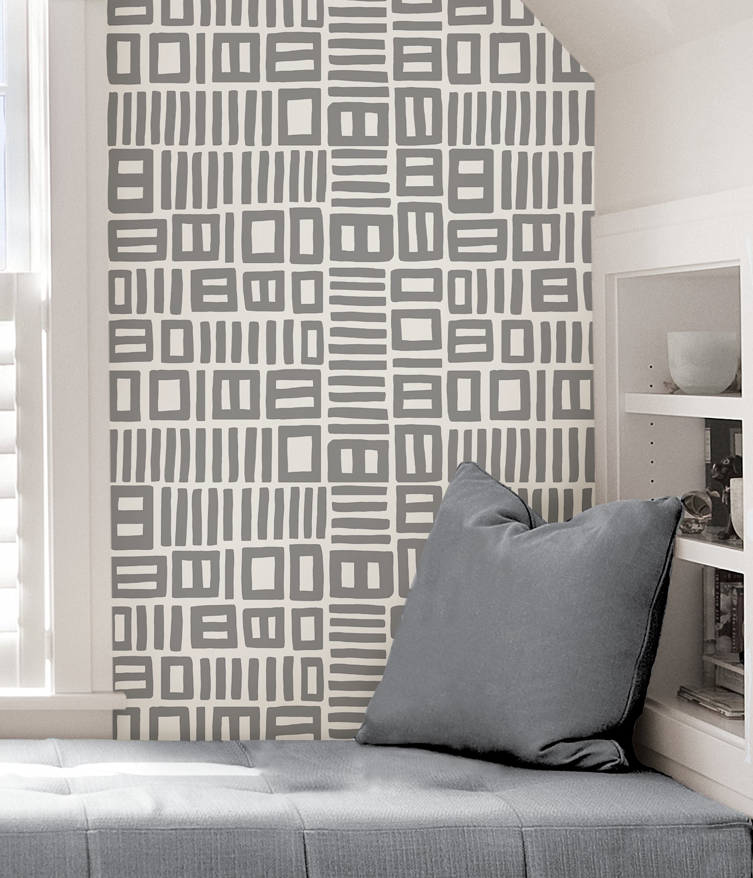 Beneath dark gray cabinets, a backsplash is enhanced with WallPops Black Pepper Paperie Traverse Peel and Stick Wallpaper, showcasing a bold geometric gray and white square pattern reminiscent of striking wallpaper. On the white countertop sit three white canisters with wooden lids alongside a large white bowl filled with green apples.