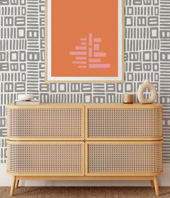 Beneath dark gray cabinets, a backsplash is enhanced with WallPops Black Pepper Paperie Traverse Peel and Stick Wallpaper, showcasing a bold geometric gray and white square pattern reminiscent of striking wallpaper. On the white countertop sit three white canisters with wooden lids alongside a large white bowl filled with green apples.