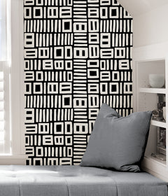 Beneath dark gray cabinets, a backsplash is enhanced with WallPops Black Pepper Paperie Traverse Peel and Stick Wallpaper, showcasing a bold geometric gray and white square pattern reminiscent of striking wallpaper. On the white countertop sit three white canisters with wooden lids alongside a large white bowl filled with green apples.