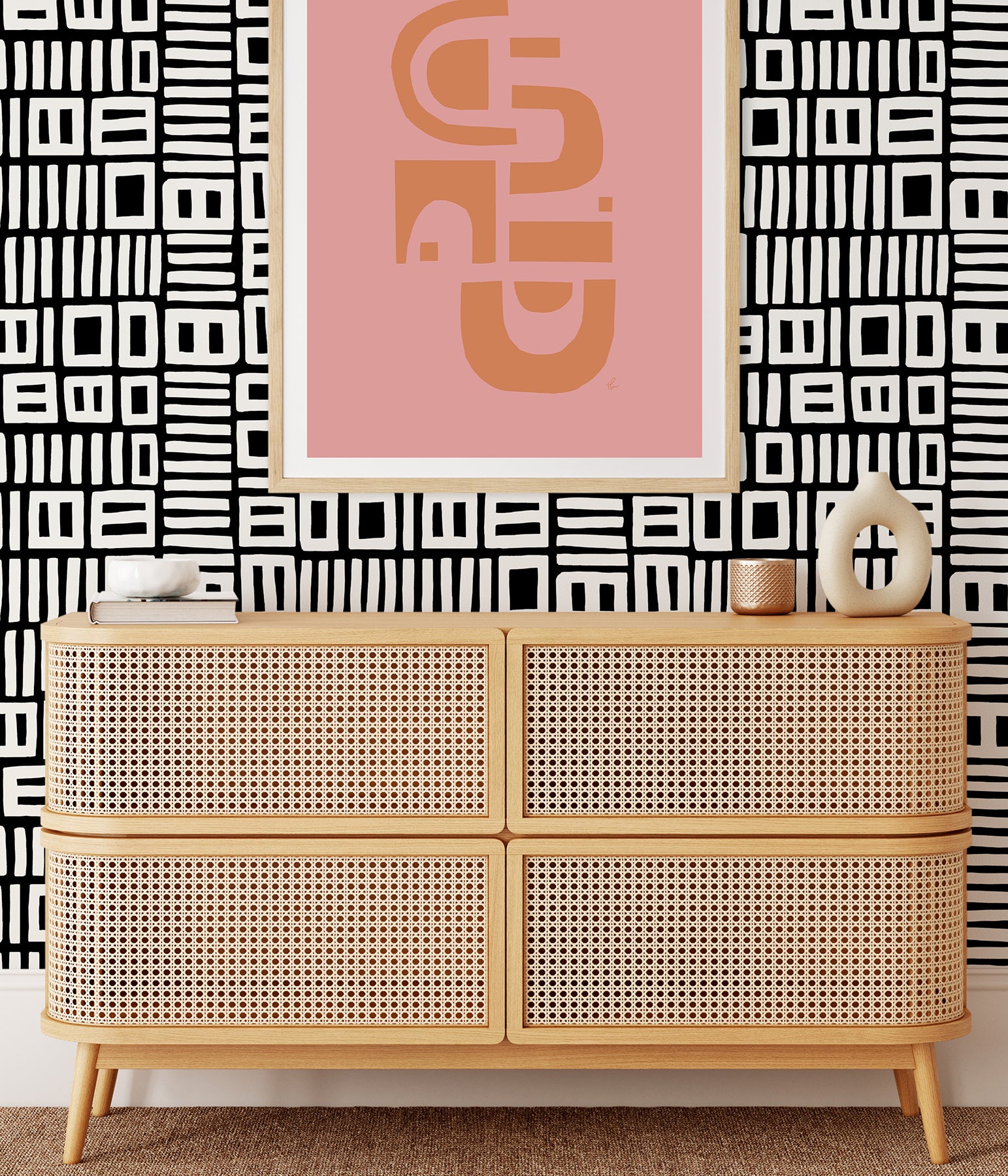Beneath dark gray cabinets, a backsplash is enhanced with WallPops Black Pepper Paperie Traverse Peel and Stick Wallpaper, showcasing a bold geometric gray and white square pattern reminiscent of striking wallpaper. On the white countertop sit three white canisters with wooden lids alongside a large white bowl filled with green apples.