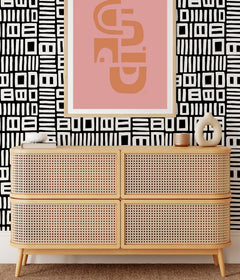 Beneath dark gray cabinets, a backsplash is enhanced with WallPops Black Pepper Paperie Traverse Peel and Stick Wallpaper, showcasing a bold geometric gray and white square pattern reminiscent of striking wallpaper. On the white countertop sit three white canisters with wooden lids alongside a large white bowl filled with green apples.