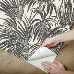 A dense, black and white grunge-style illustration of overlapping cassava palm leaves fills the image, with a light background and distressed textures that give a vintage, weathered appearance—evoking the timeless look of WallPops’ Egypt Sherrod Cassava Palm Peel and Stick Wallpaper. No blank spaces are visible in the pattern.
