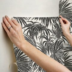 A dense, black and white grunge-style illustration of overlapping cassava palm leaves fills the image, with a light background and distressed textures that give a vintage, weathered appearance—evoking the timeless look of WallPops’ Egypt Sherrod Cassava Palm Peel and Stick Wallpaper. No blank spaces are visible in the pattern.
