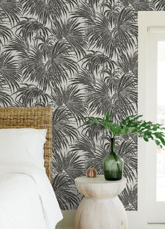 A dense, black and white grunge-style illustration of overlapping cassava palm leaves fills the image, with a light background and distressed textures that give a vintage, weathered appearance—evoking the timeless look of WallPops’ Egypt Sherrod Cassava Palm Peel and Stick Wallpaper. No blank spaces are visible in the pattern.
