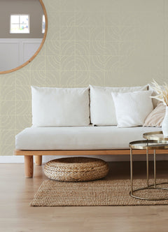 A person’s hands peel back a corner of WallPops Egypt Sherrod Batik Blok Peel and Stick Wallpaper, featuring abstract curved lines on a beige background, revealing its adhesive backing. The wallpaper rests on a wooden surface, and the person wears a ring on their left hand.