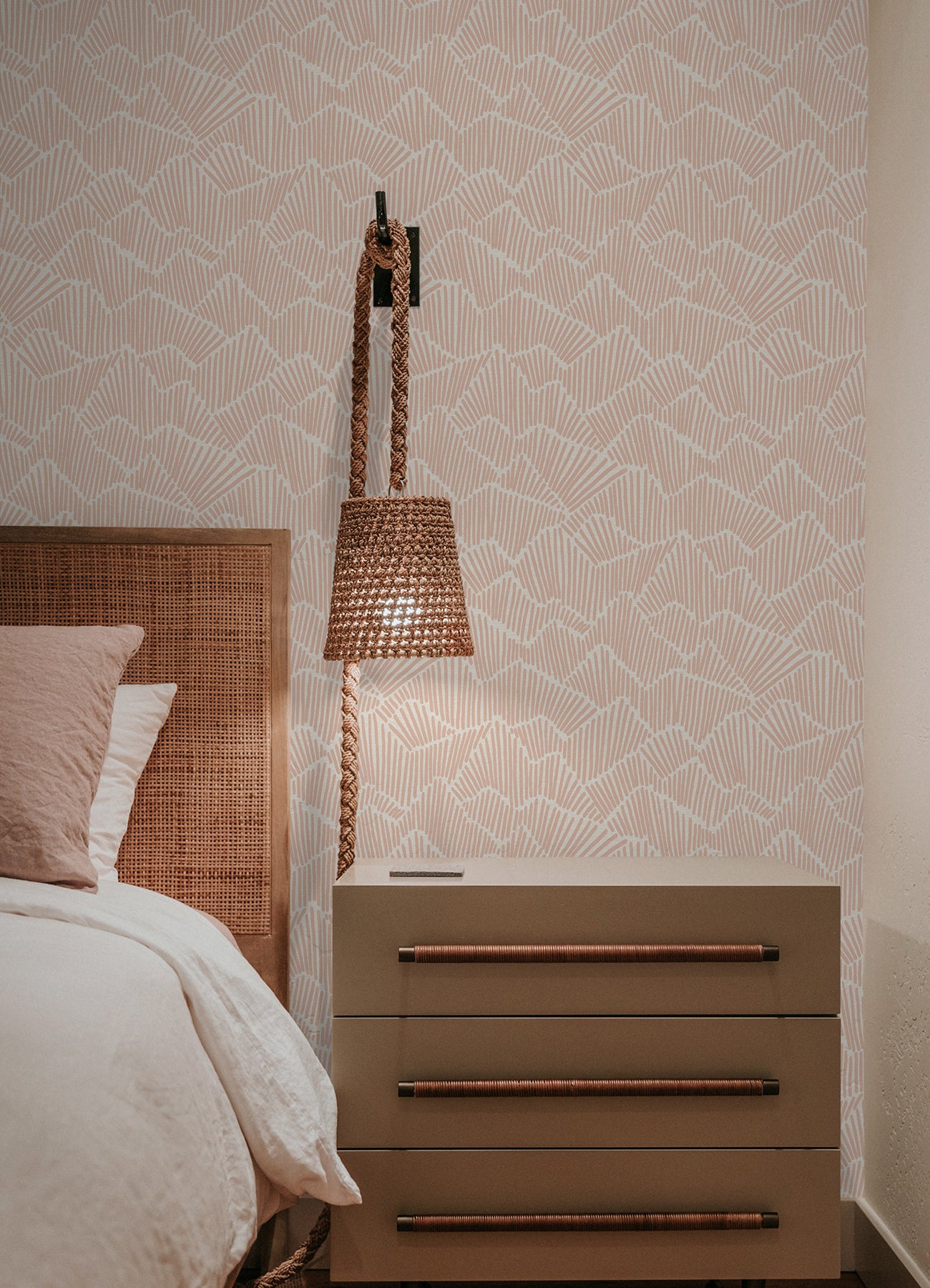 Two hands peel back a sheet of WallPops Egypt Sherrod Ridge & Valley Peel and Stick Wallpaper, which features a white abstract geometric line pattern on a beige background. The wallpaper is partially lifted from a wooden surface, and the person’s left hand is adorned with a ring.