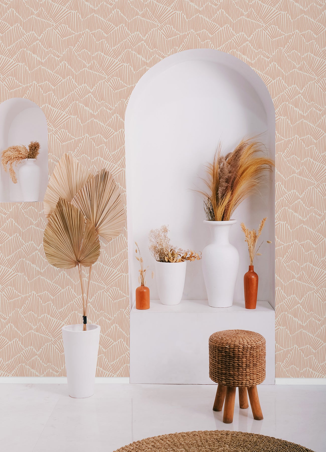 Two hands peel back a sheet of WallPops Egypt Sherrod Ridge & Valley Peel and Stick Wallpaper, which features a white abstract geometric line pattern on a beige background. The wallpaper is partially lifted from a wooden surface, and the person’s left hand is adorned with a ring.