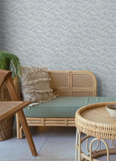 Two hands peel back a sheet of WallPops Egypt Sherrod Ridge & Valley Peel and Stick Wallpaper, which features a white abstract geometric line pattern on a beige background. The wallpaper is partially lifted from a wooden surface, and the person’s left hand is adorned with a ring.