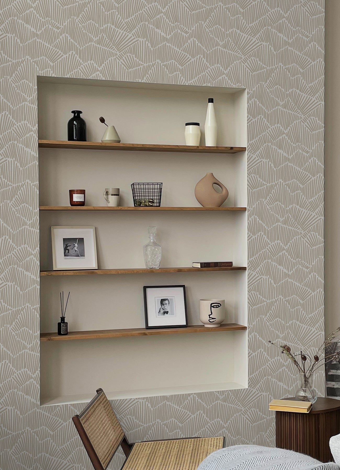 Two hands peel back a sheet of WallPops Egypt Sherrod Ridge & Valley Peel and Stick Wallpaper, which features a white abstract geometric line pattern on a beige background. The wallpaper is partially lifted from a wooden surface, and the person’s left hand is adorned with a ring.