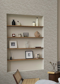 Two hands peel back a sheet of WallPops Egypt Sherrod Ridge & Valley Peel and Stick Wallpaper, which features a white abstract geometric line pattern on a beige background. The wallpaper is partially lifted from a wooden surface, and the person’s left hand is adorned with a ring.
