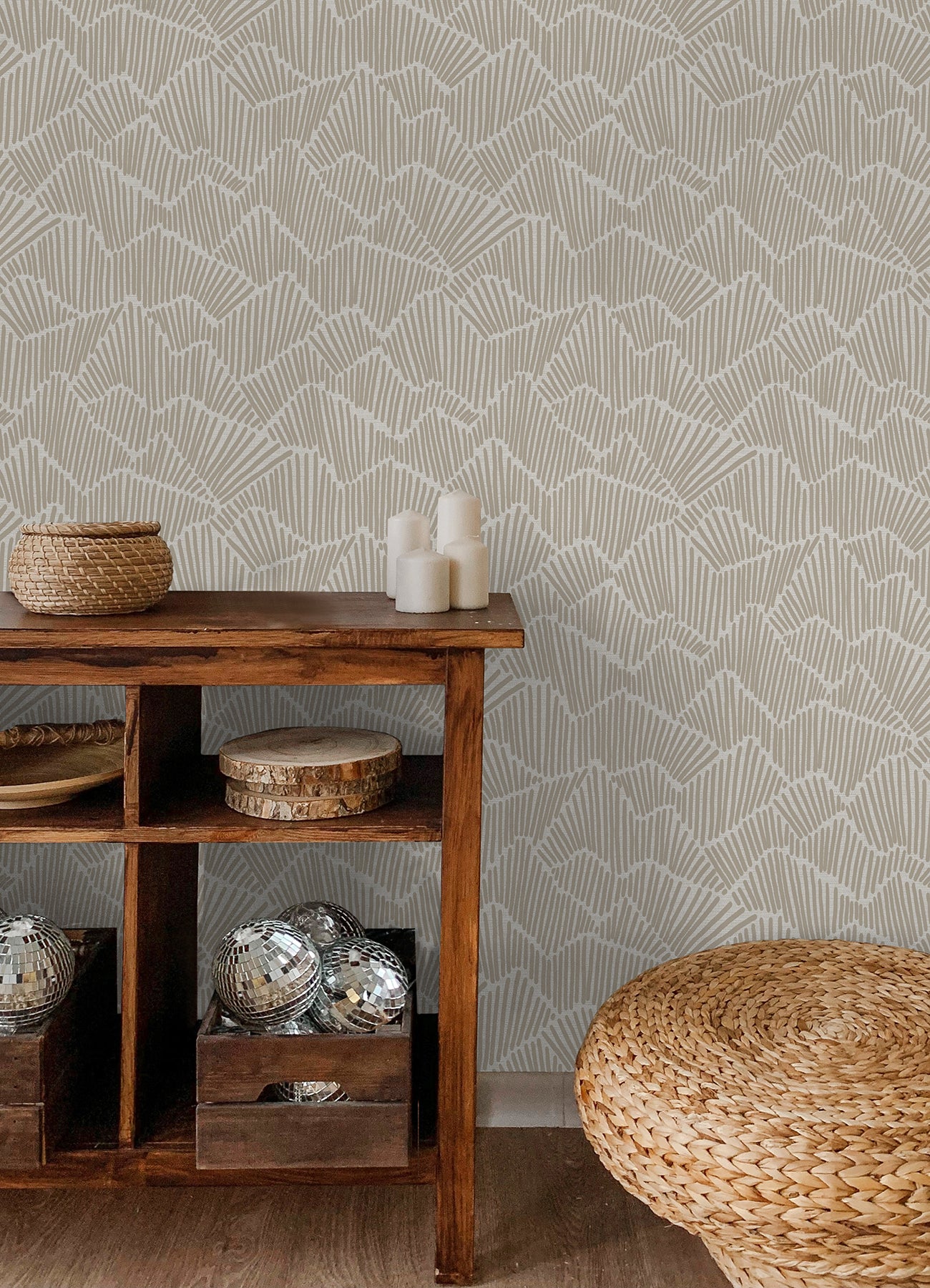 Two hands peel back a sheet of WallPops Egypt Sherrod Ridge & Valley Peel and Stick Wallpaper, which features a white abstract geometric line pattern on a beige background. The wallpaper is partially lifted from a wooden surface, and the person’s left hand is adorned with a ring.