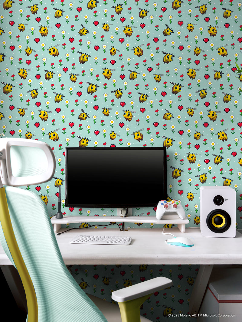 A sleek gaming setup with a white desk, computer monitor, keyboard, mouse, speakers, and a controller. A modern white and mint chair faces the desk. The wall features Minecraft-themed pixel art wallpaper with bees, flowers, and hearts on a teal background.