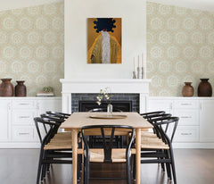 A modern dining room featuring a wooden table, eight black chairs, white built-in cabinets, and blue LiLi WhittWhitt Harmony Peel and Stick Wallpaper by WallPops. Above a white fireplace hangs a colorful abstract portrait. The space is accented with decorative pottery, candles, and a single-stem vase.