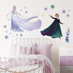 WallPops Frozen 2 Anna, Elsa, and Olaf Purple Wall Decals feature Anna in a black cape and green dress beside Olaf the snowman and Elsa with her shimmering gown among purple and blue snowflakes, a bird, and rustic accents on a white background.
