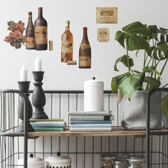 WallPops Wine Tasting Wall Decals package comes with 56 charming peel and stick decals featuring a delightful wine and kitchen motif. The sample image shows bottles, jars, and glasses arranged artfully on a kitchen counter, making them a perfect match for rustic interiors. These easy-to-apply wall decals are visible through the packaging window, offering an ideal way to bring countryside charm to your space.