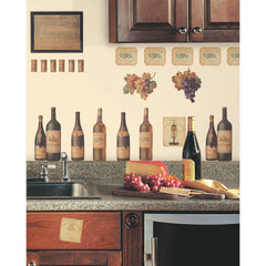 WallPops Wine Tasting Wall Decals package comes with 56 charming peel and stick decals featuring a delightful wine and kitchen motif. The sample image shows bottles, jars, and glasses arranged artfully on a kitchen counter, making them a perfect match for rustic interiors. These easy-to-apply wall decals are visible through the packaging window, offering an ideal way to bring countryside charm to your space.