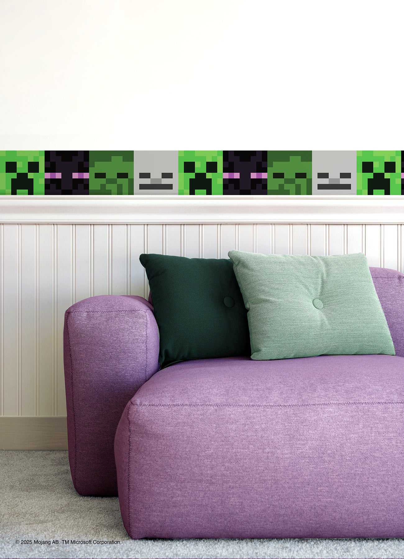 A purple couch with green cushions sits against a white wall decorated with Minecraft Hostile Mobs Wall Decals, featuring peel and stick borders with pixelated creeper faces and other in-game mobs.