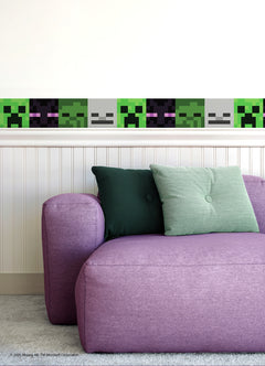 A purple couch with green cushions sits against a white wall decorated with Minecraft Hostile Mobs Wall Decals, featuring peel and stick borders with pixelated creeper faces and other in-game mobs.