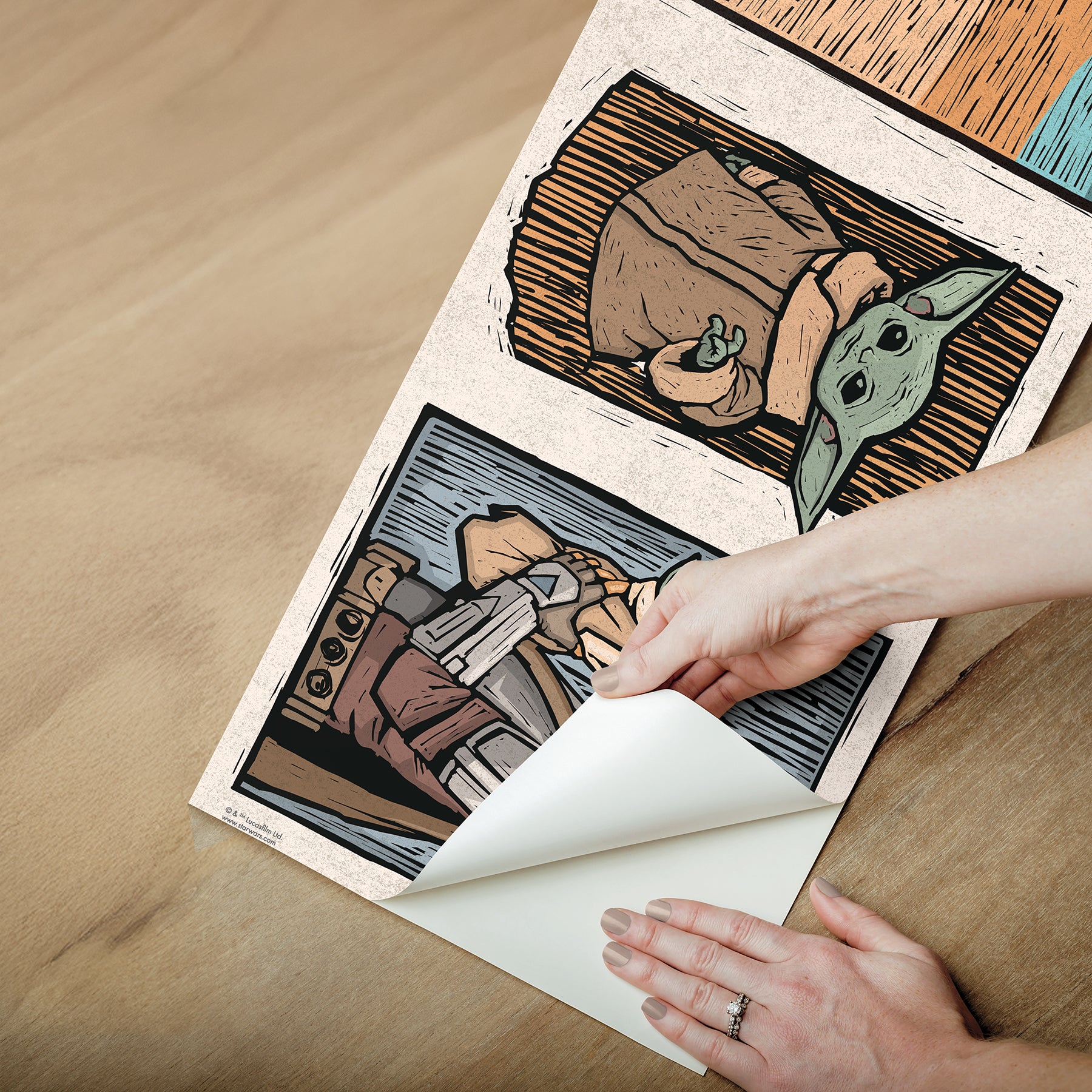 A white decorative rocket stands on a wooden shelf beside white books. Below are two beige storage bins. Behind, a light blue wall features a border of whimsical Star Wars The Mandalorian and Grogu linocut illustrations created with WallPops peel and stick wall decals. The scene is neatly arranged and playful.
