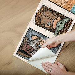 A white decorative rocket stands on a wooden shelf beside white books. Below are two beige storage bins. Behind, a light blue wall features a border of whimsical Star Wars The Mandalorian and Grogu linocut illustrations created with WallPops peel and stick wall decals. The scene is neatly arranged and playful.