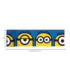 A person wearing a silver ring on their hand peels the backing off a large sticker resembling the WallPops Universal Studios Minions Always Eyeconic Border. The sticker features part of a cartoon character with yellow skin, round eyes, and black goggles set against a blue and yellow background, all laid out on a wooden surface.