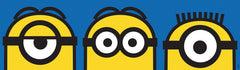 A person wearing a silver ring on their hand peels the backing off a large sticker resembling the WallPops Universal Studios Minions Always Eyeconic Border. The sticker features part of a cartoon character with yellow skin, round eyes, and black goggles set against a blue and yellow background, all laid out on a wooden surface.