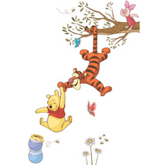 Winnie the Pooh dangles from Tigger’s tail, reaching for a falling honey pot, while Tigger hangs upside down from a tree branch as Piglet looks on above. Blue and red butterflies flutter nearby, and daisies grow below, creating a cheerful scene. The Disney Winnie the Pooh Swinging for Honey Giant Wall Decals by WallPops features these charming characters with rustic design elements—perfect for peel and stick wall decals or as accents on distressed barn wood décor to bring warmth to any room.