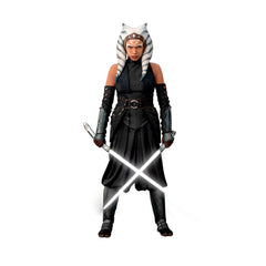 A striking silhouette of Ahsoka Tano, clad in black armor with blue and white striped head-tails and facial markings, stands confidently holding two crossed white lightsabers—her arms wrapped in dark gauntlets—against a plain white background. The Star Wars Ahsoka Peel and Stick Giant Wall Decal by WallPops is an inspiring way to add bold character to any room.