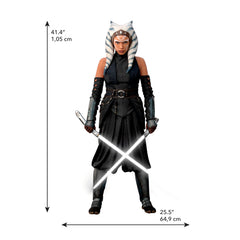 A striking silhouette of Ahsoka Tano, clad in black armor with blue and white striped head-tails and facial markings, stands confidently holding two crossed white lightsabers—her arms wrapped in dark gauntlets—against a plain white background. The Star Wars Ahsoka Peel and Stick Giant Wall Decal by WallPops is an inspiring way to add bold character to any room.