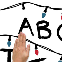 The WallPops Netflix Stranger Things Christmas Lights Peel And Stick Giant Wall Decals With Alphabet features a hand-drawn alphabet arranged in three rows, each row displayed beneath a line of colorful Christmas lights and accented with circled numbers 1–8 along the lines. This rustic design, measuring 27.43 69.6 cm tall by 46.04 1.16 m wide, boasts a light gray background reminiscent of distressed barn wood for added character.