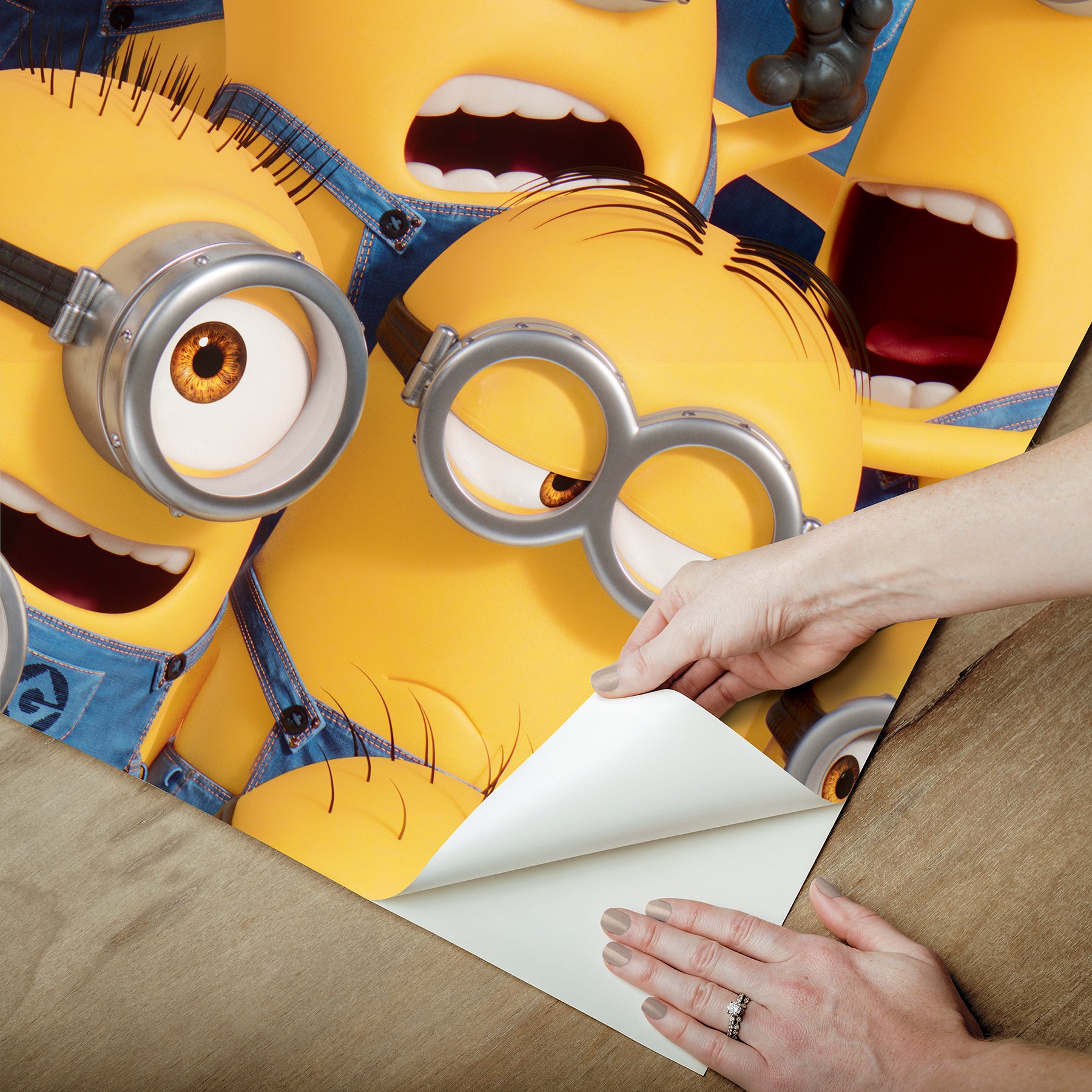 A lively scene from the Universal Studios Minions One in a Minion Peel and Stick Mural by WallPops shows a crowd of small yellow Minions—complete with goggles, blue overalls, and unique expressions—gathered closely together. Some are grinning, others appear surprised or are calling out, all adding to the playful and chaotic energy of this mural.