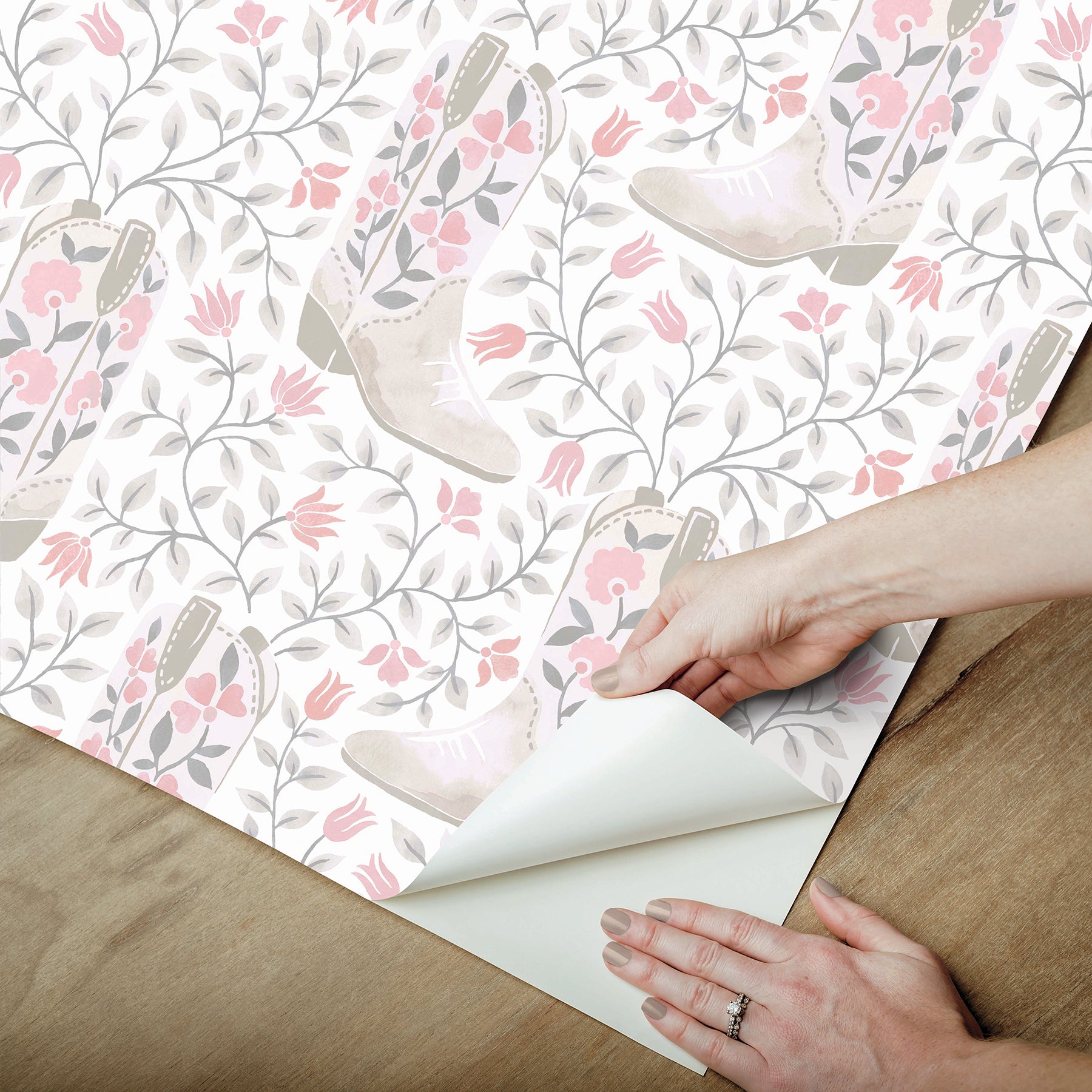 Introducing the Cowgirl Like Me Peel and Stick Wallpaper by WallPops—this seamless wallpaper showcases pale beige cowboy boots accented with delicate floral motifs, all arranged against a light backdrop interwoven with winding leafy vines and dainty blossoms. The soft, muted illustration style lends a subtle vintage charm, making it the ideal choice for anyone seeking adorable cowgirl-inspired décor.