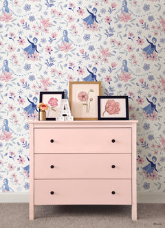 Hands with a silver ring smooth Frozen II Frozen 2 Anna and Elsa Floral Peel and Stick Wallpaper by WallPops onto a cream wall, aligning its repeating pink floral pattern and cartoon girls in blue dresses.