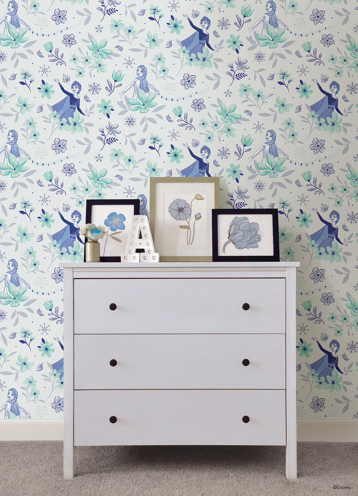 Hands with a silver ring smooth Frozen II Frozen 2 Anna and Elsa Floral Peel and Stick Wallpaper by WallPops onto a cream wall, aligning its repeating pink floral pattern and cartoon girls in blue dresses.