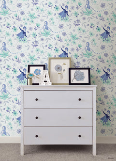 Hands with a silver ring smooth Frozen II Frozen 2 Anna and Elsa Floral Peel and Stick Wallpaper by WallPops onto a cream wall, aligning its repeating pink floral pattern and cartoon girls in blue dresses.