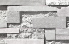 A grayscale photo features a wall covered with WallPops Mineral Siding Adhesive Film, designed to mimic staggered rectangular bricks. The film displays a variety of surfaces: some areas are smooth, while others have rough textures or subtle floral engravings, creating striking contrasts in patterns and finishes. Soft lighting casts gentle shadows, highlighting the realistic relief of the Mineral Siding design.