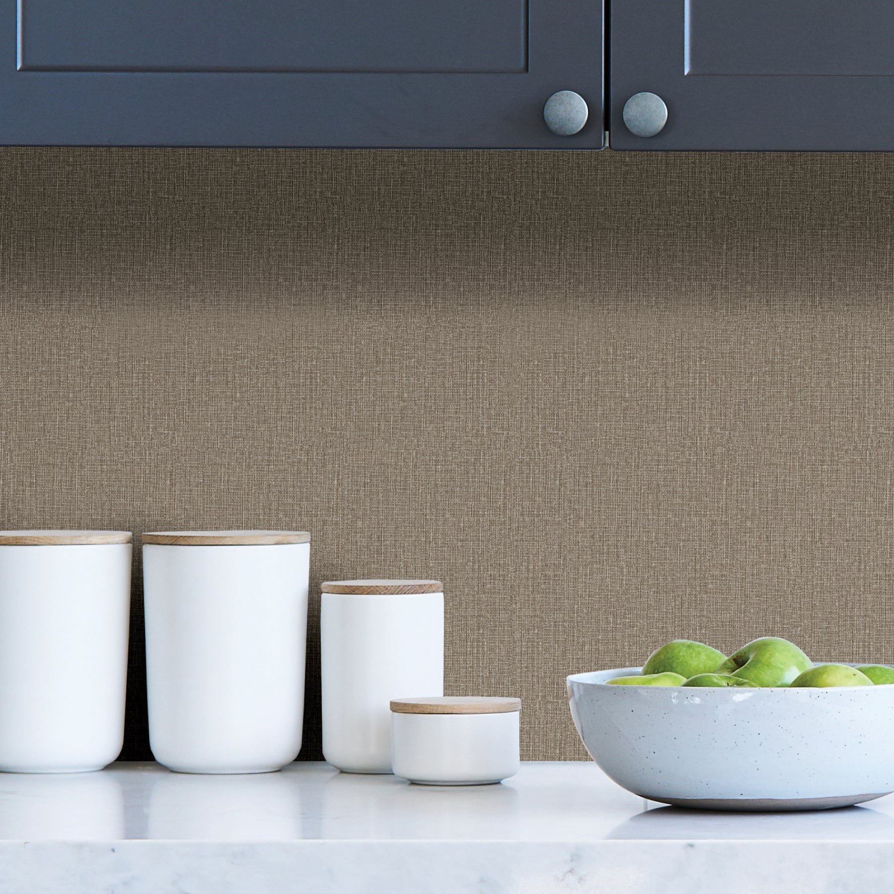 A close-up of WallPops Natural Linen Adhesive Film reveals a beige textured surface with a subtle woven pattern of fine intersecting lines and slight irregularities, creating a soft and natural aesthetic. The uniform, neutral color gives the adhesive film a calm and understated appearance.