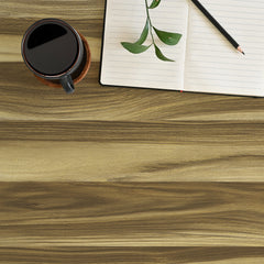 A black coffee cup rests on a surface covered with WallPops Modern Wood Adhesive Film in a light brown color, next to an open notebook with a pen and a small green plant placed on its page; the lower portion of the image displays empty table space showcasing the stylish film.