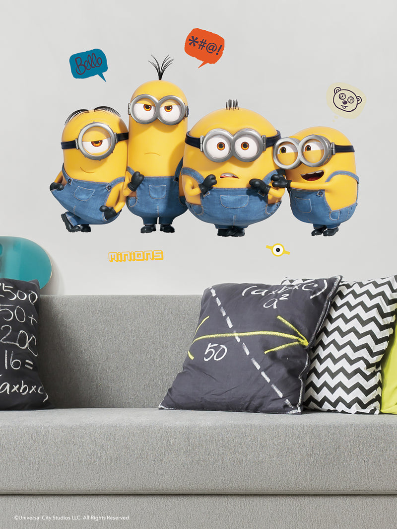 Four Minions, wearing blue overalls and goggles, pose on a wall above a grey couch with black-and-white math-themed pillows. Speech bubbles show Bello, symbols, and a bear face. The Minions display mixed emotions.