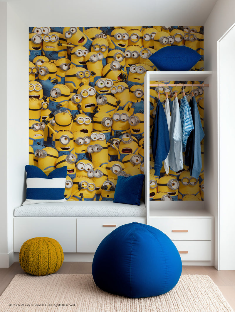 A cozy, modern room features a vibrant Minions wall mural, blue and white pillows, a yellow knitted pouf, a blue beanbag, and an open closet with hanging clothes. The decor is playful, with white furniture and wooden accents.