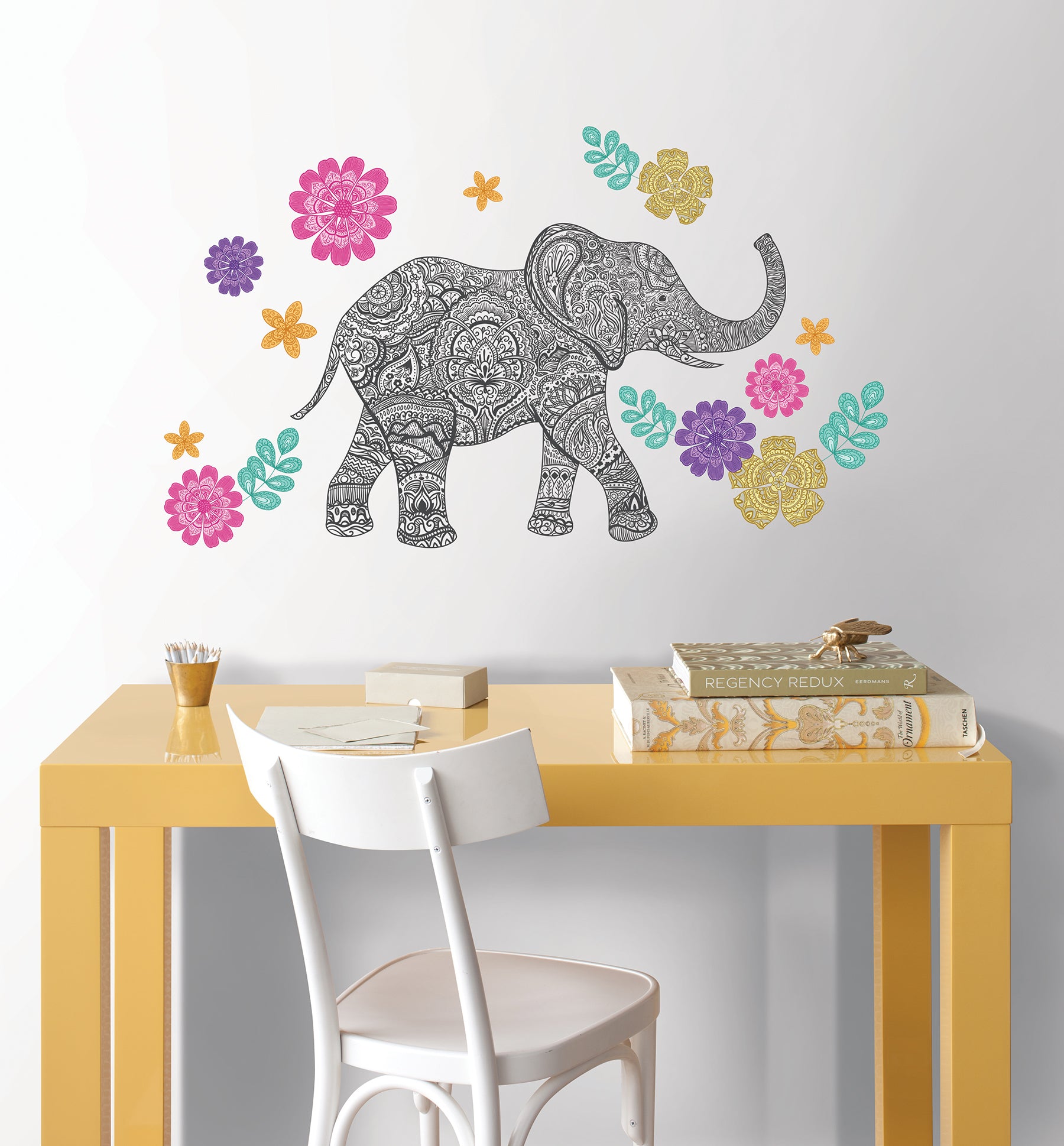 Bring vibrant artistry to your space with the WallPops Mehndi Small Wall Art Kits. This kit features a highly detailed black and white elephant illustration adorned with ornate designs, standing right amidst an array of intricate, colorful flowers in pink, yellow, orange, purple, and teal hues, complemented by lush green leaves on a crisp white background.