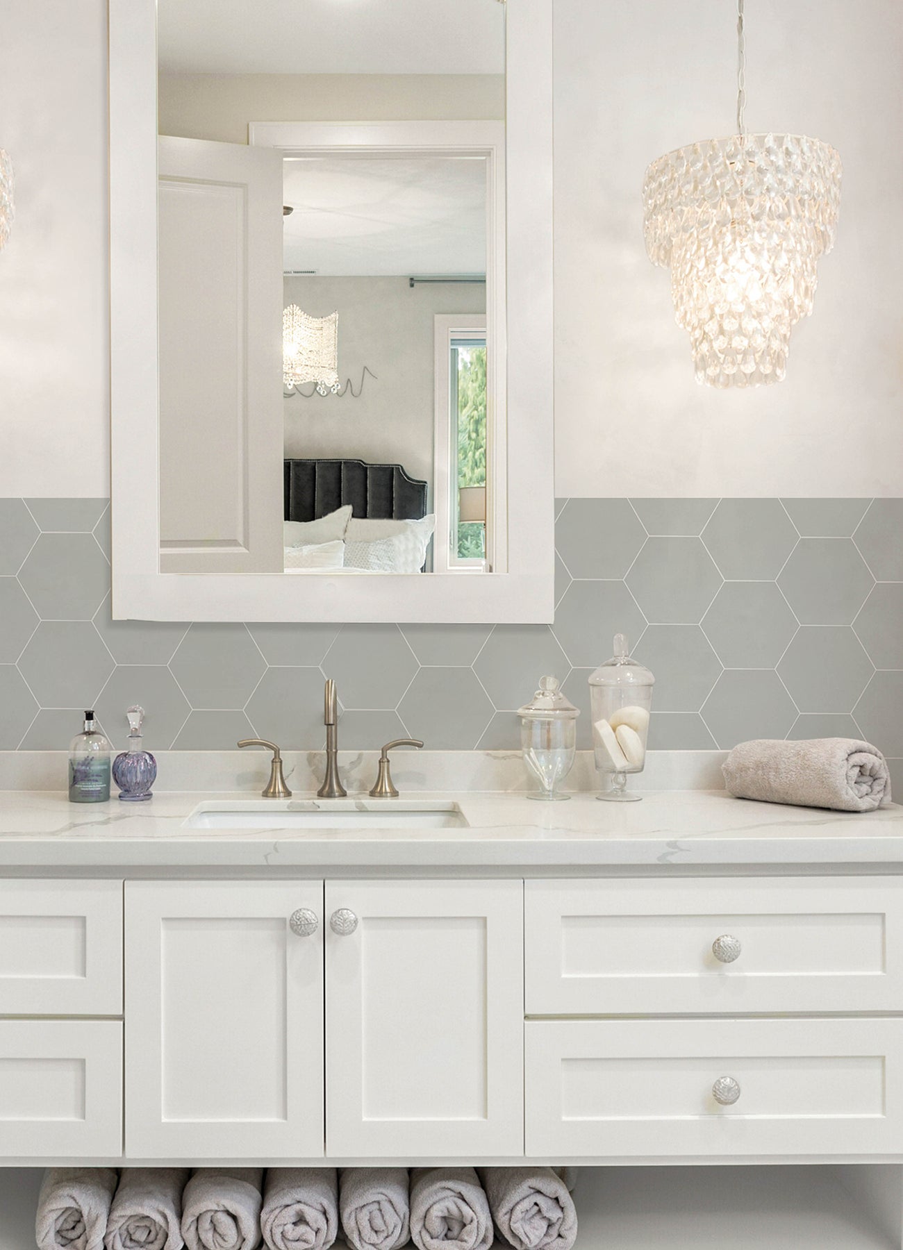 Modern kitchen featuring a white countertop, wooden stools with round seats and black footrests, a green backsplash made of WallPops Hexagon Peel & Stick Luxury Wall Tiles, light wood flooring, and a white backsplash. A blue pot and plants decorate the stove and counter. The space is illuminated by bright natural light from two windows.