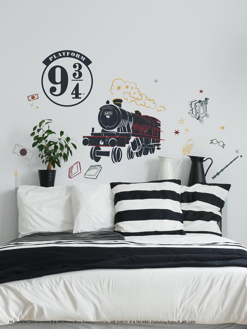 A white bed with black-striped pillows sits against a wall decorated with a Hogwarts Express train mural, the Platform 9¾ sign, and various Harry Potter-themed illustrations like glasses, broomstick, scarf, and flying letters, plus a potted plant on a bedside table.